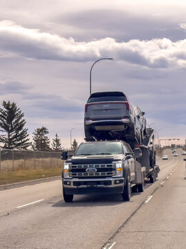 Calgary, Alberta, Canada. April 15, 2026. A Ford Super Duty car hauler transports a new Kia SUV on a highway under a cloudy sky.