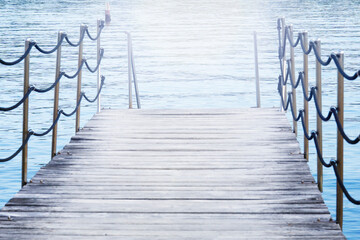 Naklejka premium wooden pier bridge blue calm water surface rope railing bright sun light effect on lake horizon with copy space for banner design concept of travel, tourism, architecture