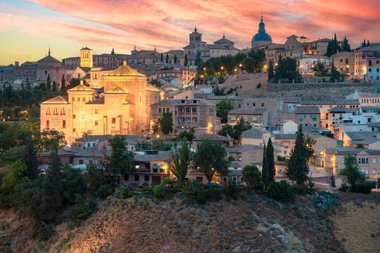 The city of Toledo glows with a warm, golden light as the sun sets behind its historic stone buildings and tiered hillside architecture.