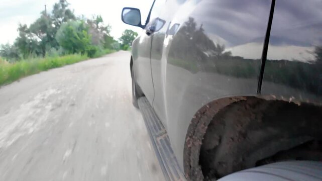A car travels over a rough dirt road in a countryside area. There are trees on either side of the path and the sky looks cloudy. The journey shows the road conditions.