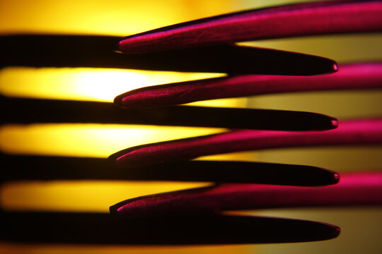 Tenedores met&aacute;licos dispuestos en superposici&oacute;n, iluminados con  luces amarillas y magenta que generan un efecto abstracto. Las l&iacute;neas repetitivas de los dientes crean un patr&oacute;n visual con sombras.   