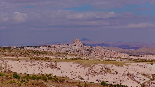 Aerial drone view of Uchisar Castle rising above Cappadocia landscape in Turkey, surrounded by unique rock formations and valleys under a dramatic cloudy sky