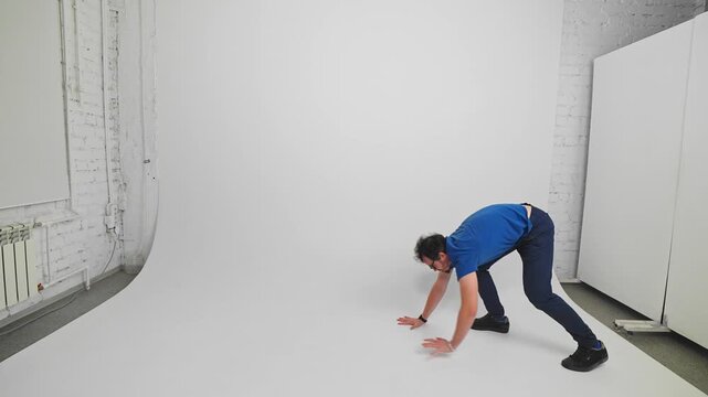 Man is casual clothes is walking on his fours leaning on his hands filmed in a studio in slow motion. Young adult Caucasian guy is imagining that he is animal showcasing it by gait. Dynamic movement