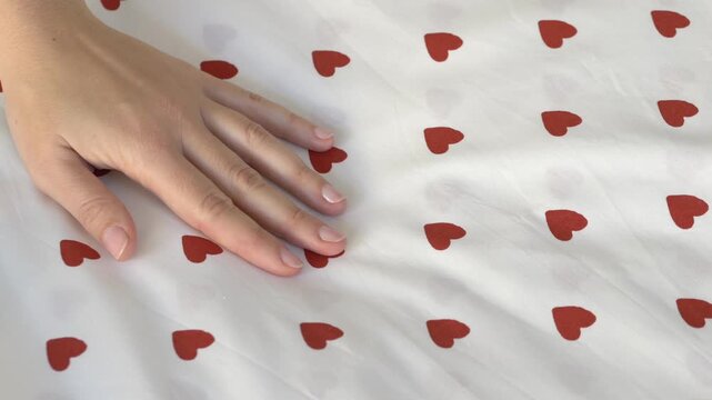 Female hand touching soft fabric with heart pattern. Cozy home textile concept, child bedding or bedsheet material, comfort and softness in everyday interior lifestyle. Concept of home, bedding fabric