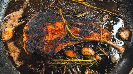 Fototapeta premium Pork cutlet searing in a pan with garlic and rosemary, steam rising. Crispy golden crust and juicy interior highlight a rich cooking process and gourmet meat concept.