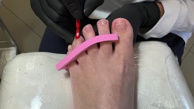 Pedicure podology salon beauty toenails polish feet care procedure with red nail application by gloved specialist during professional foot treatment and cosmetic grooming.