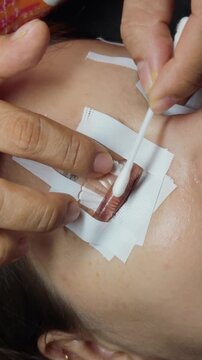 Woman receiving a lash lift as a beautician applies perming solution with a cotton swab to curl and define natural eyelashes in a salon close up beauty treatment scene