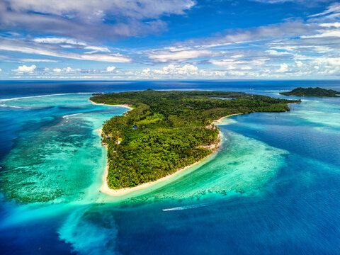Aerial view of Sipura Island featuring lush tropical forests, vibrant turquoise coral reefs, and pristine white sand beaches in Mentawai Islands Regency, West Sumatra, Indonesia.