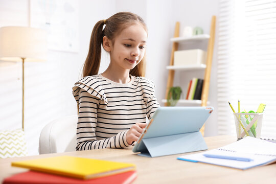 Cute girl with tablet doing homework at table indoors