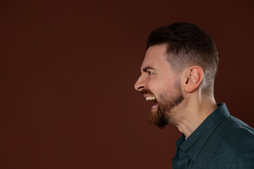Obraz premium Portrait of angry man screaming on brown background. Space for text