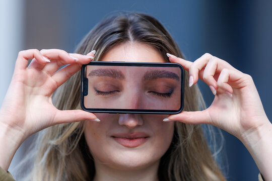 Woman holds smartphone with image of closed eyes in front of her face while smiling