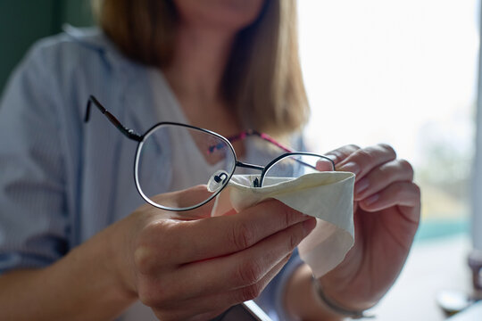Woman cleaning eyeglasses with cloth while holding frame in hands