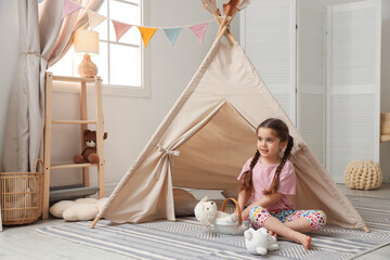 Little girl playing with toys near toy wigwam in playroom, space for text © New Africa