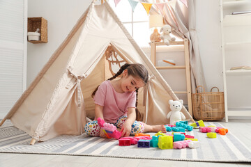 Little girl playing with building blocks near toy wigwam in playroom © New Africa