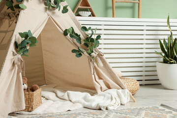Cute wigwam with leaves and blanket in stylish child's room. Space for text © New Africa
