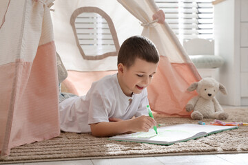 Little boy drawing in sketchbook near toy wigwam at home © New Africa
