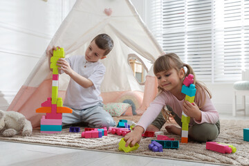 Little kids playing with building blocks near toy wigwam at home © New Africa