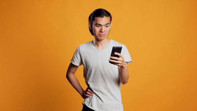 Young male model browsing internet on mobile phone, scrolling through social media app on smartphone. Modern smiling person using telephone in studio, online website or browser.