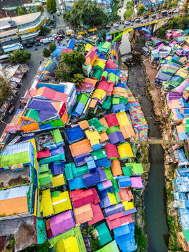 Aerial view of the vibrant Kampung Warna Warni Jodipan with multicolored rooftops along the river in Kecamatan Blimbing, Jawa Timur, Indonesia.