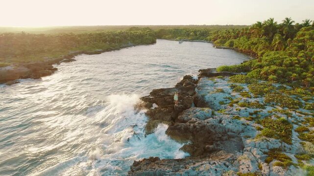 Aerial view of rocky tropical coast and woman walking near lagoon at sunset