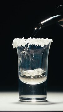 Mexican Tequila Mezcal pouring with lime and salt on a stone table. Strong vodka rum alcoholic drink is poured from a bottle into a shots.