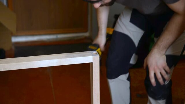 A man with works in his workshop. Profession carpenter. A man works with a tree. The carpenter takes drills holes wooden products in a bright workshop. Carpentry, craftsmanship, handwork concept.