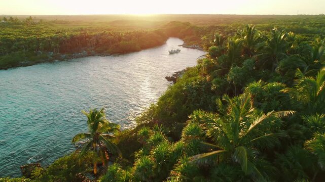 Boat anchored in tropical lagoon surrounded by dense jungle at golden sunset