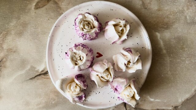 A top view of tulip-shaped marshmallows with berry swirls and a red heart symbol on a white plate