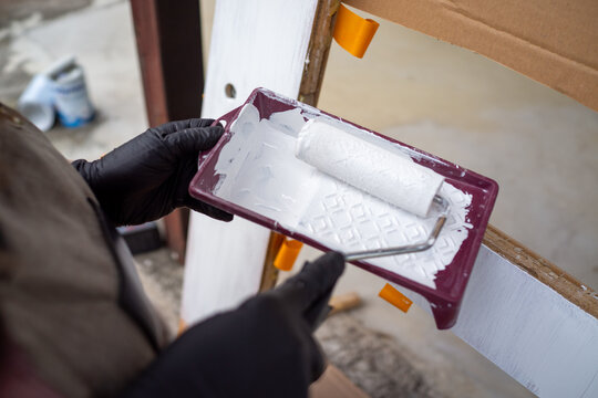 Applying white paint onto textured surface. Home renovation prep showing painting tools and techniques