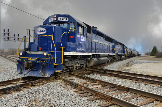 After departing a local Michigan railroad yard, Great Lakes Central Railroad locomotives power a freight train through a double diamond crossing of the Canadian National mainline tracks.