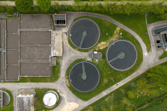 Aerial view of a water treatment plant featuring circular clarifiers and rectangular aeration tanks surrounded by green vegetation in San Giovanni Valdarno, Tuscany, Italy.