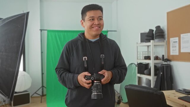 Man photographer holds camera and checks settings while smiling in studio with green backdrop and softbox; contentment creativity craft.
