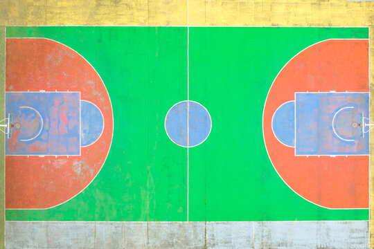 Aerial view of a colorful outdoor basketball court with vibrant green, orange, and blue painted surfaces and weathered textures in San Giovanni Valdarno, Tuscany, Italy.