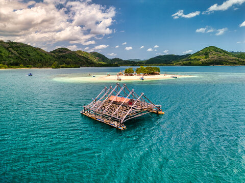 Aerial view of Gili Kedis island and a traditional floating fishing platform on turquoise water in Sekotong, West Nusa Tenggara, Indonesia.