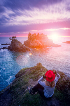 Rear view of a woman sitting on a cliff looking at sea stacks at sunset, Samuel H Boardman State Park, Oregon, USA
