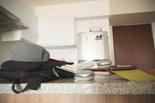 Backpack, hat, books, and headphones waiting on a kitchen counter in a home study setup