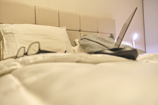 Cozy bed acting as a remote workstation with a laptop and eyeglasses