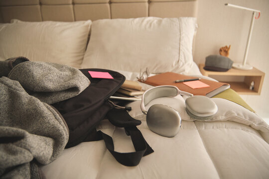 Backpack, headphones, and study items resting on a neat white bed in a bedroom
