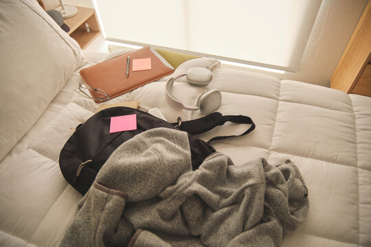 Backpack, headphones, and laptop sleeve resting on a cozy bed, ready for a study session