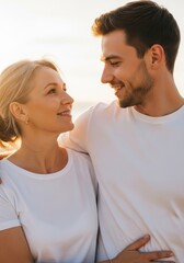 Obraz premium Loving couple embracing at sunset. Romantic man and woman in white t-shirts gazing affectionately outdoors. Beachside affection in warm golden hour light for relationship stock photo