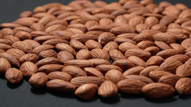 Large quantity of raw almonds shot from a tilted perspective on a dark background, emphasizing abundance and healthy diet.