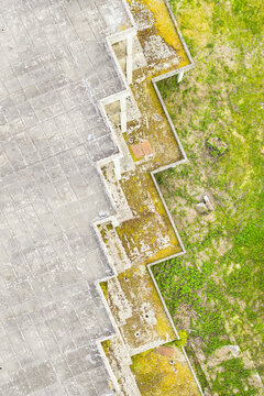 Aerial view of the geometric concrete roof and weathered zig-zag edges of a modern building surrounded by green grass in Leccio, Toscana, Italy.