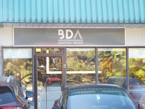 Nepean, Ontario, Canada &ndash; July 27, 2025: The "BDA Lighting Group" storefront features a gray horizontal sign, large glass windows reflecting trees, and cars parked directly in front at 77 Auriga Dr #6