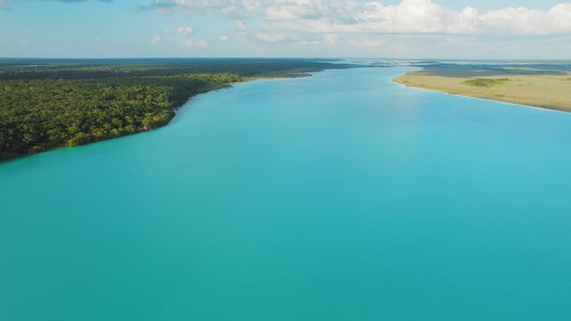Wide turquoise lagoon bordered by forest and open grassland under blue sky