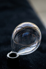 Obraz premium A fragile iridescent soap bubble attached to a small metal base against a dark background
