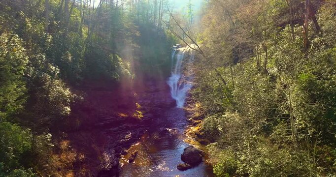 Dry Falls in North Carolina during fall season. Scenic waterfall with clear water cascading over rocky ledge surrounded by golden autumn forest