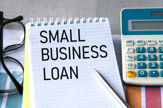 SMALL BUSINESS LOAN - words in a notebook with a calculator, glasses and pen in the background