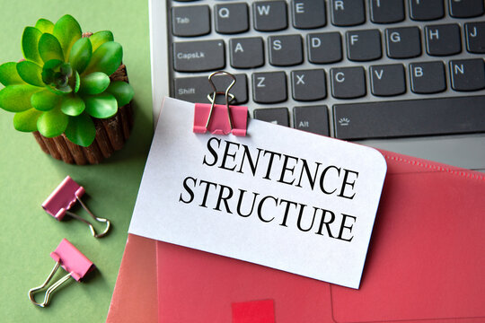 A red folder is lying on the table next to the laptop with the words SENTENCE STRUCTURE
