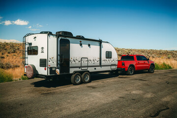 Red pickup truck towing travel trailer on desert roadside under clear blue sky © Victoria Nefedova