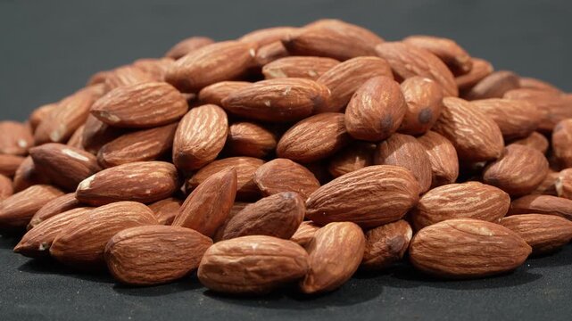 Horizontal eye-level shot of a heap of raw almonds rotating on a dark background, highlighting natural depth and healthy nutrition.